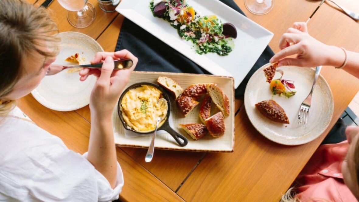 Two women eat from several plates of food.